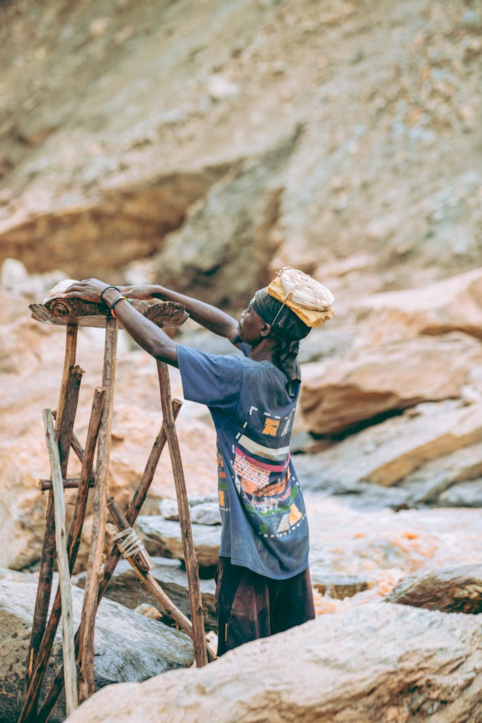 An African miner using traditional methods in a rocky outdoor setting during the day.